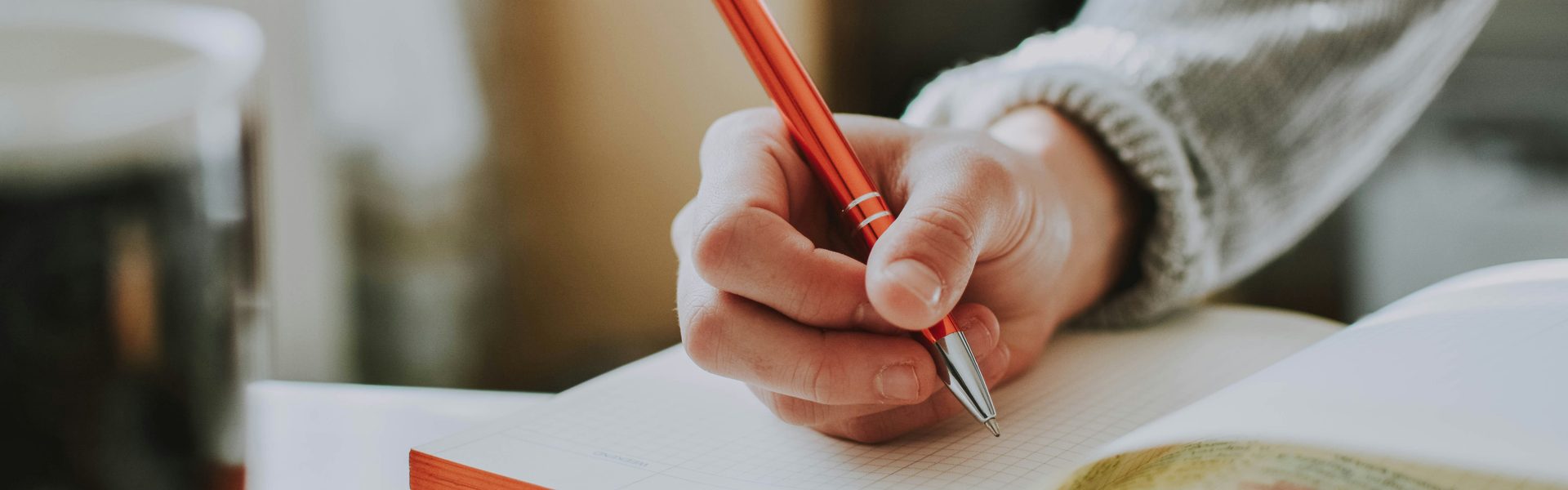 A hand writing in a notebook with an orange pen